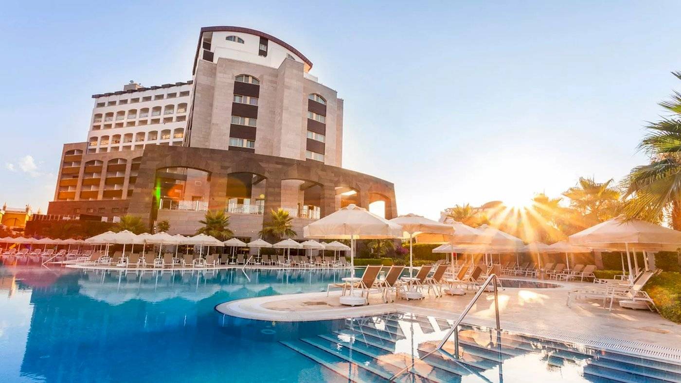 Melas Lara Hotel im Sonnenaufgang mit Swimmingpool und Sonnenschirmen.