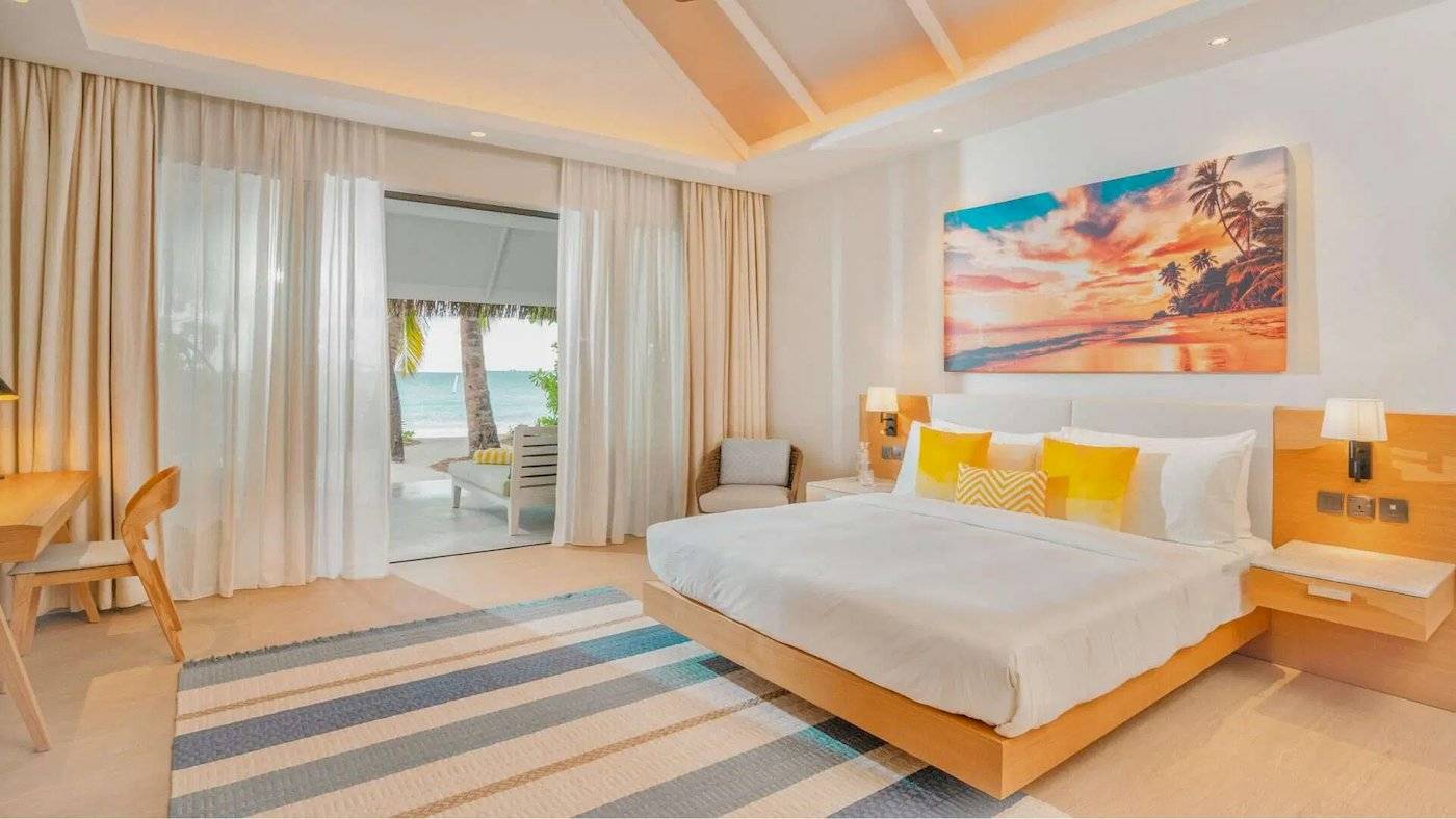 Eine Suite im Nova Maldives Hotel mit Blick auf das Meer, einem großen Bett, einem Tisch und einem Sessel.