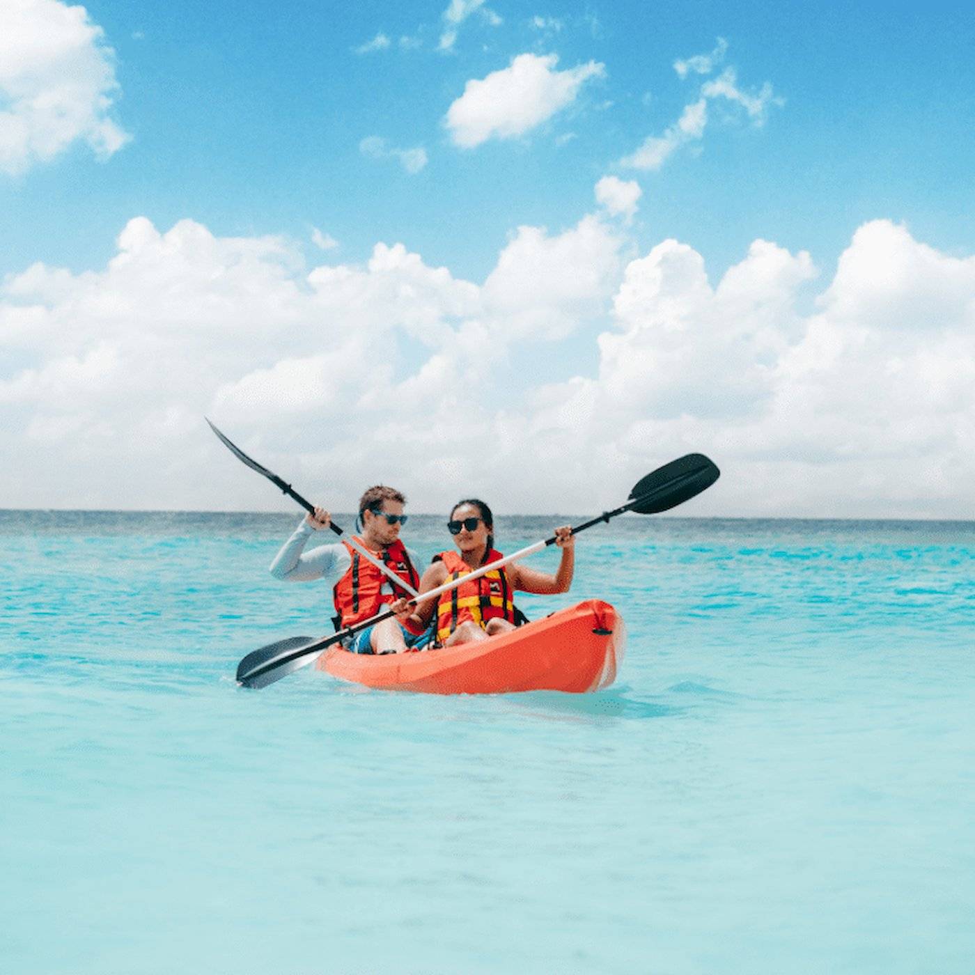 Zwei Personen paddeln in einem orangefarbenen Kajak auf dem Meer.