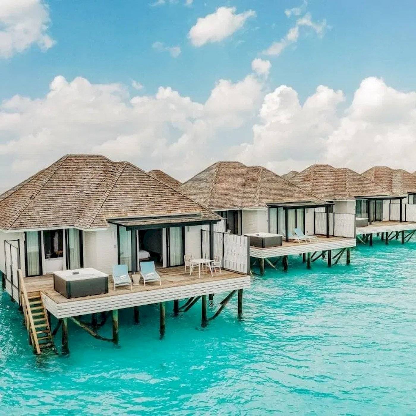 Reihe von Wasservillen im Nova Maldives Hotel mit blauem Wasser und blauem Himmel.