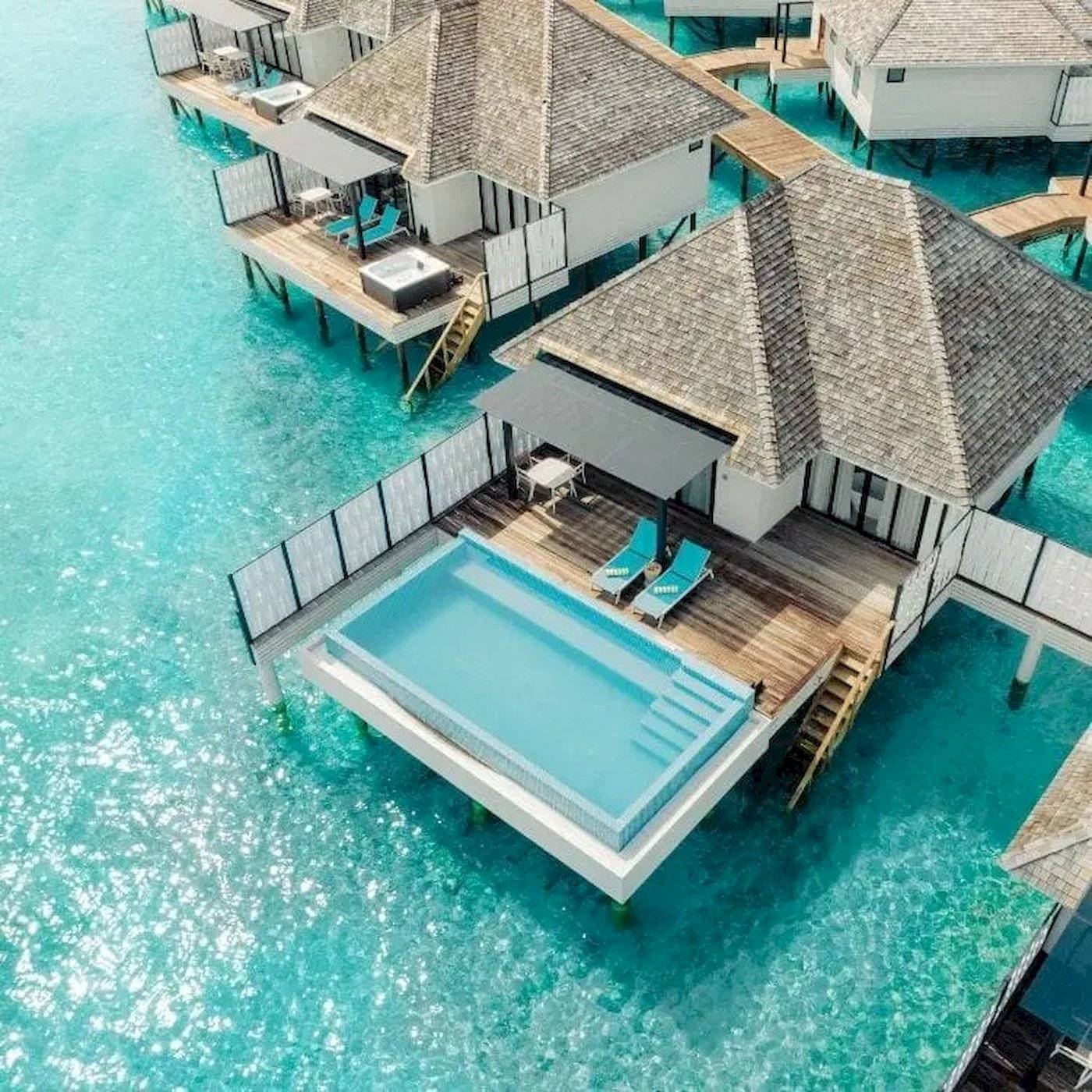 Aus der Luft aufgenommene Nova Maldives Wasservillen mit blauem Pool und Lounge-Bereich.