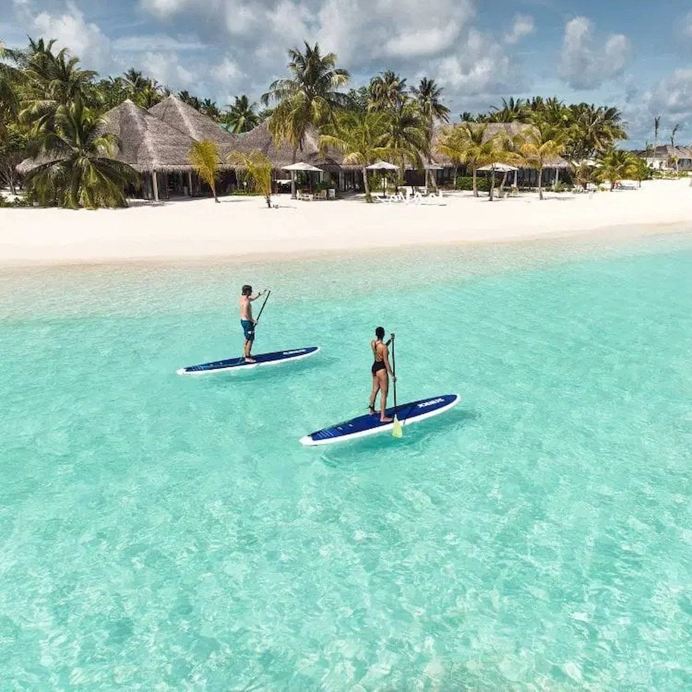 Zwei Personen paddeln auf blauen Brettern im klaren Wasser vor Nova Maldives.