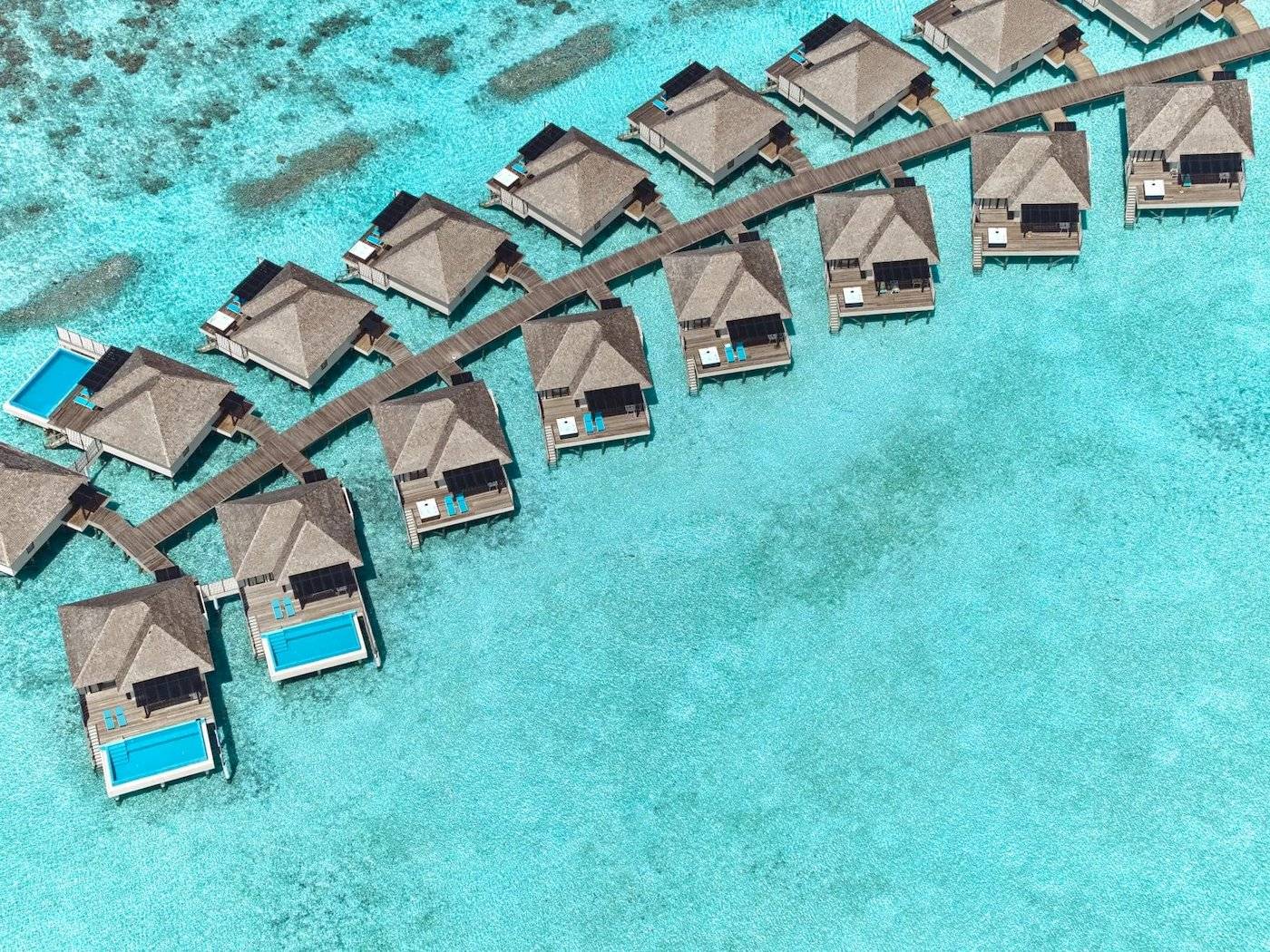 Luftaufnahme des Nova Maldives Resorts mit Wasservillen und Stegen