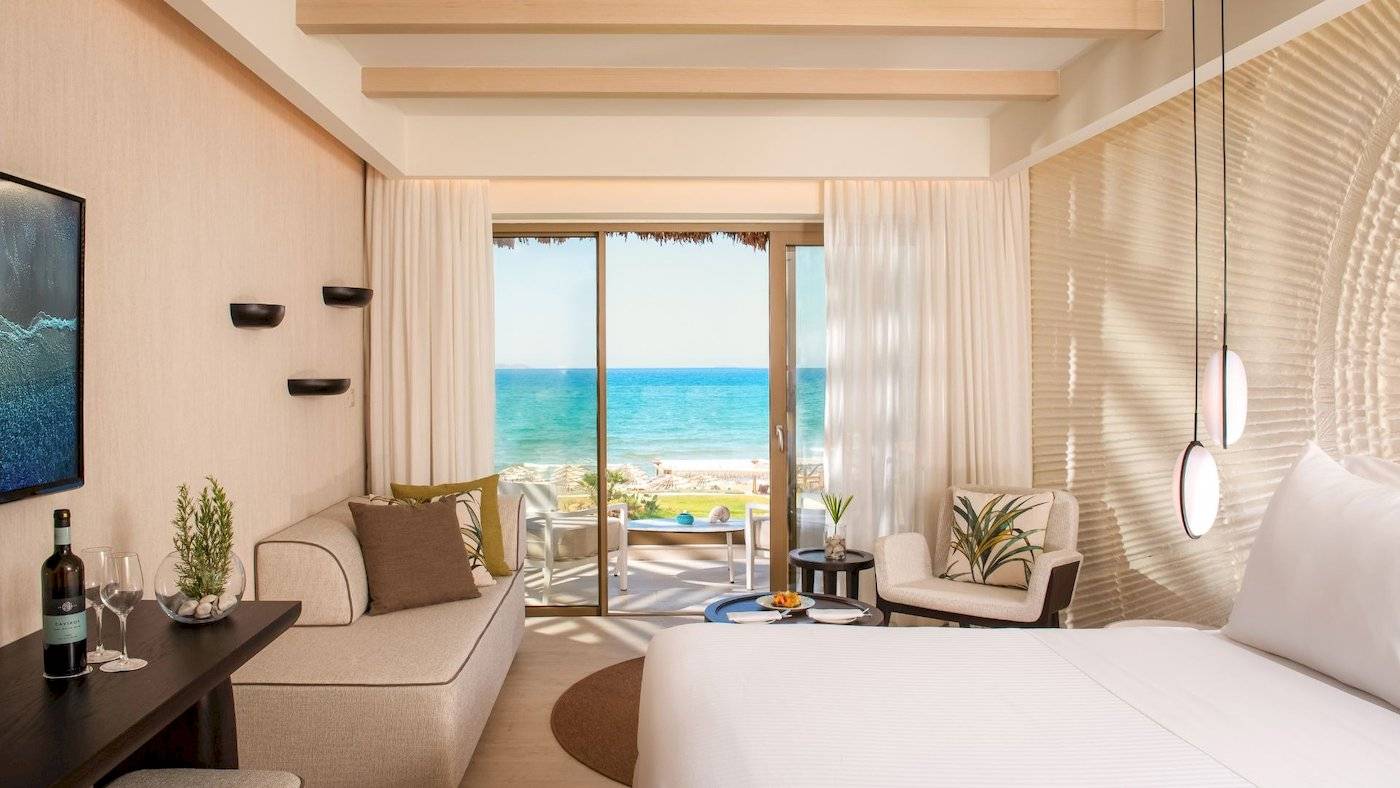 Mitsis Selection Rinela Hotel Suite mit Meerblick, großem Bett, Sofa, Tisch, Wein und Dekor.