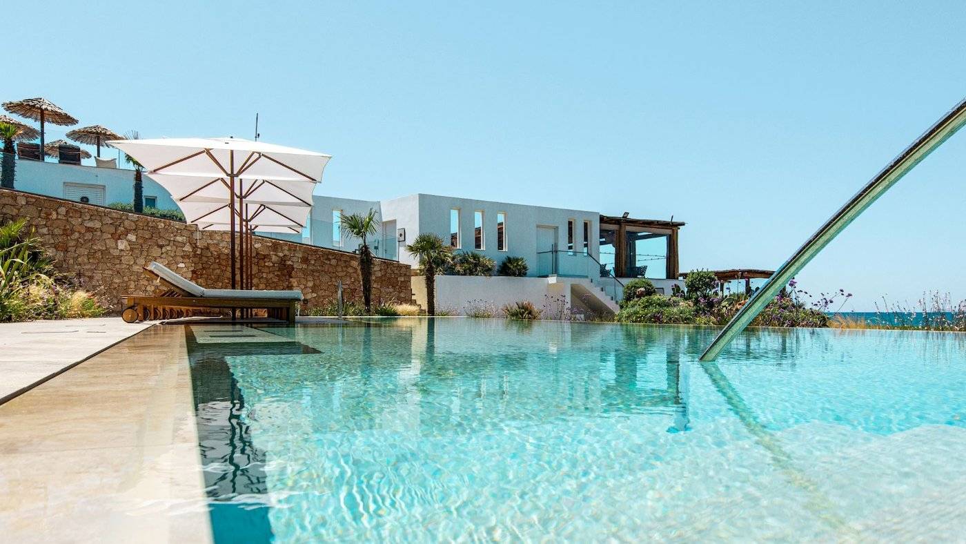 Außenpool des Mitsis Selection Rinela Hotels mit Liegestühlen und Sonnenschirmen.