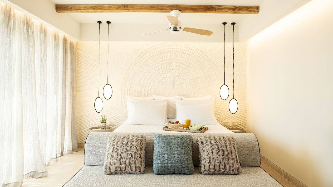 Schlafzimmer im Mitsis Selection Rinela Hotel mit Bett, Tisch, Lampen und Frühstücksplatte