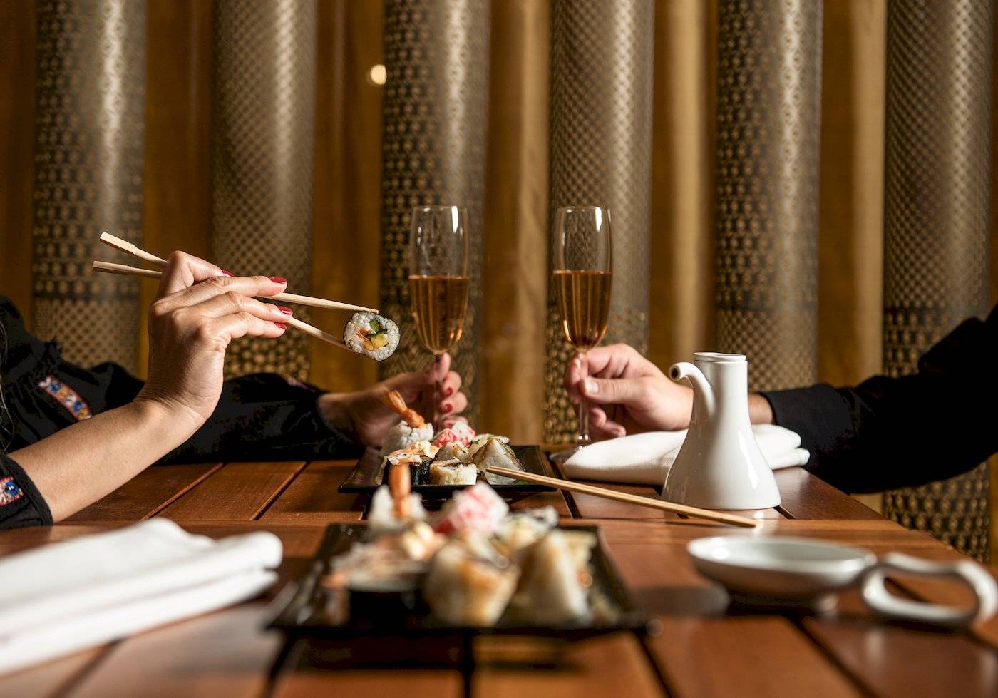 Zwei Personen sitzen an einem Tisch und essen Sushi mit Chopsticks und trinken Champagner.