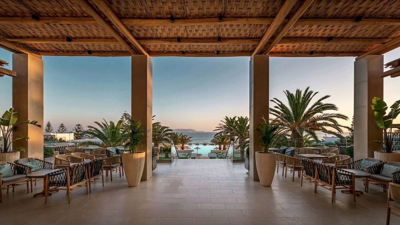 Terrasse des Mitsis Selection Rinela Hotels mit Blick auf Palmen und Meer