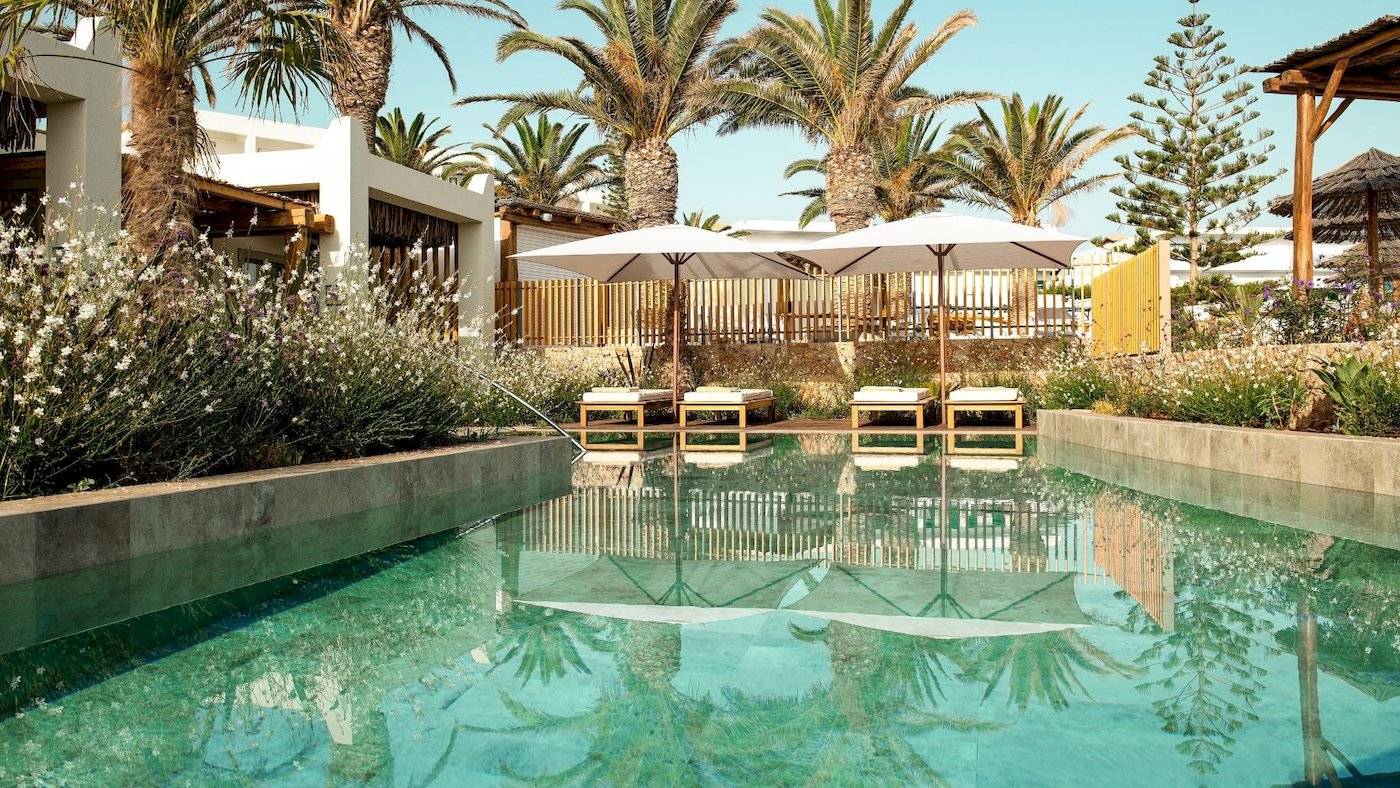 Pool im Mitsis Selection Rinela Hotel mit weißen Sonnenschirmen und Liegen.