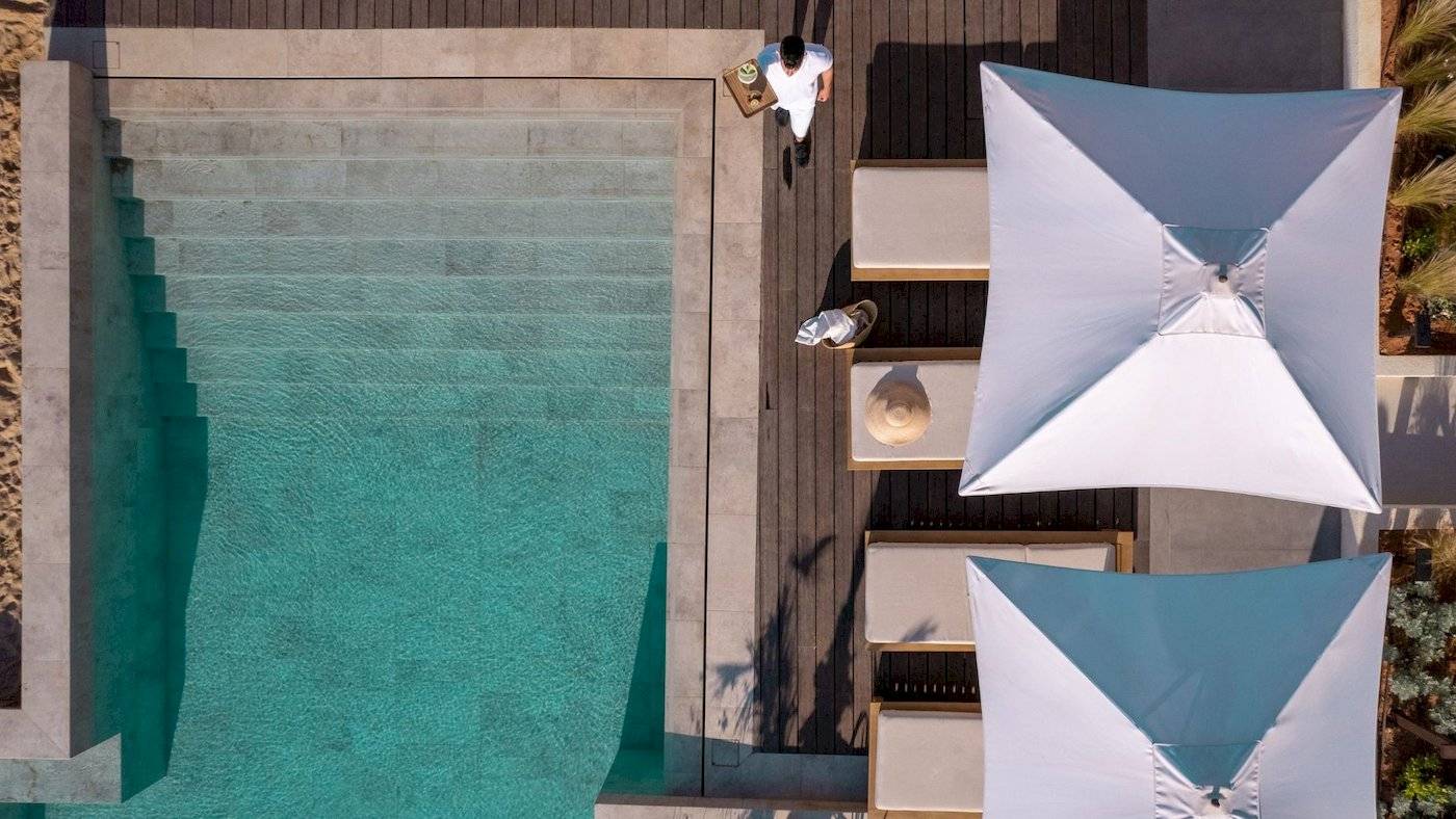 Mitsis Selection Rinela Hotel Außenbereich mit Pool, Sonnenliegen und Sonnenschirmen.