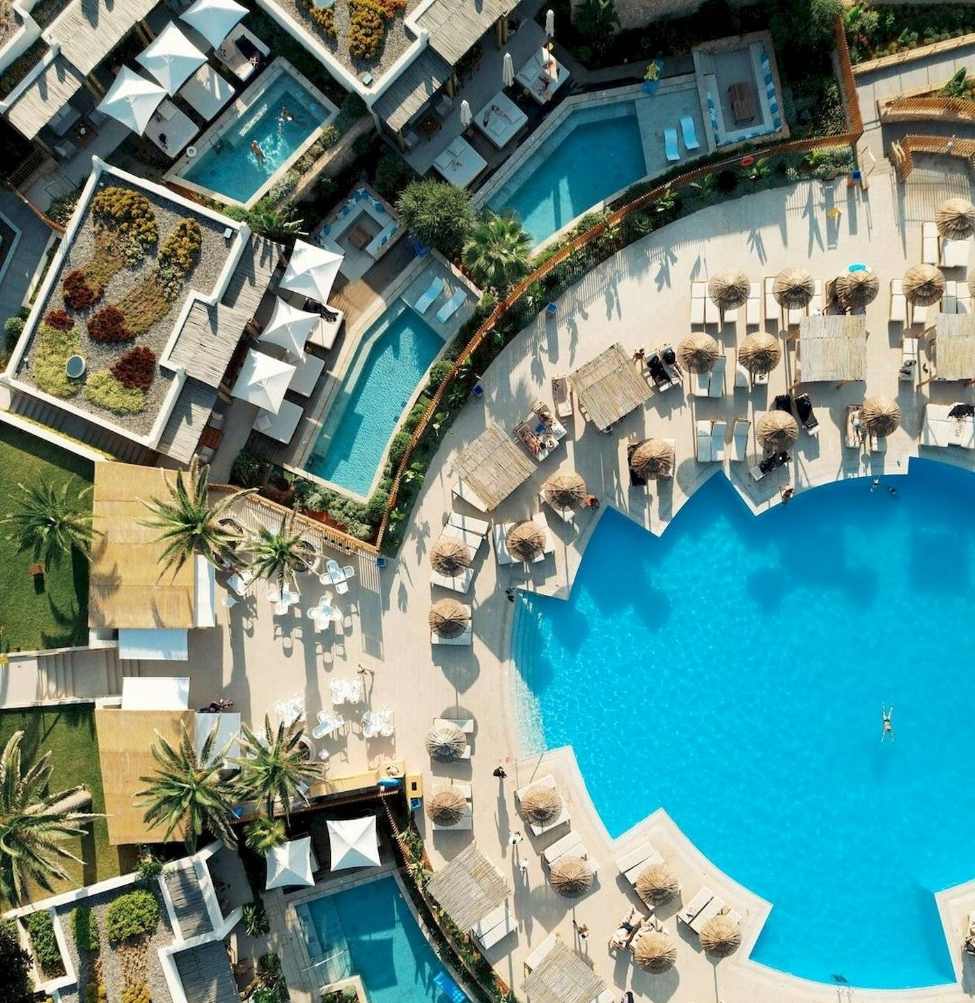 Luftaufnahme des Mitsis Selection Rinela Hotel Pools mit Liegestühlen und Sonnenschirmen.