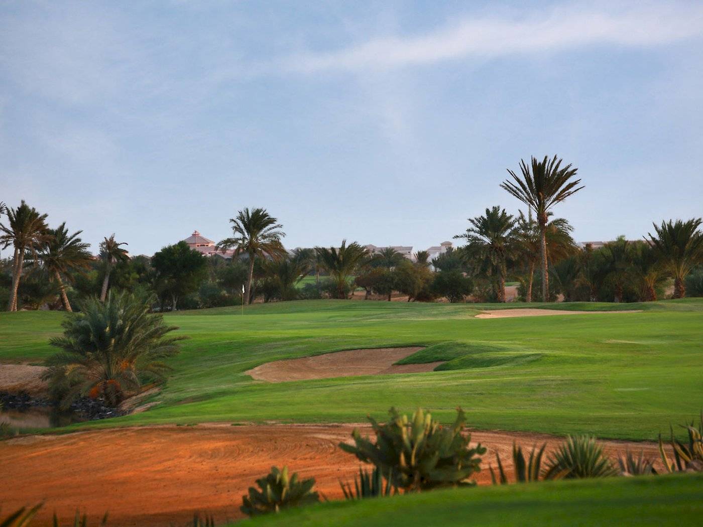 Golfplatz im Moevenpick Resort & Spa El Gouna mit gruenem Rasen und Palmen.