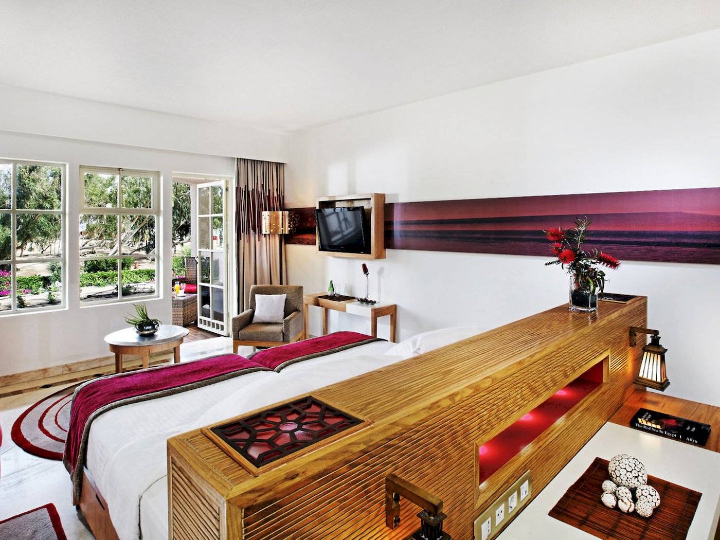 Innenansicht eines Hotelzimmers im Mövenpick Resort & Spa El Gouna mit einem Bett, Fernseher und Pflanzen.