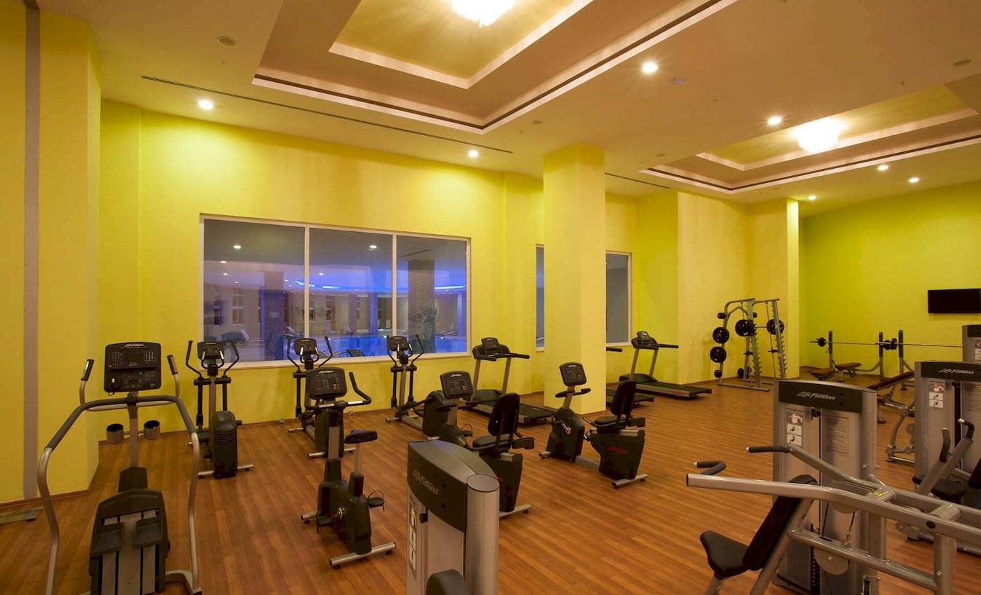 Fitness-Center im Defne Defnem Hotel mit verschiedenen Trainingsgeräten und einem Swimmingpool im Hintergrund.
