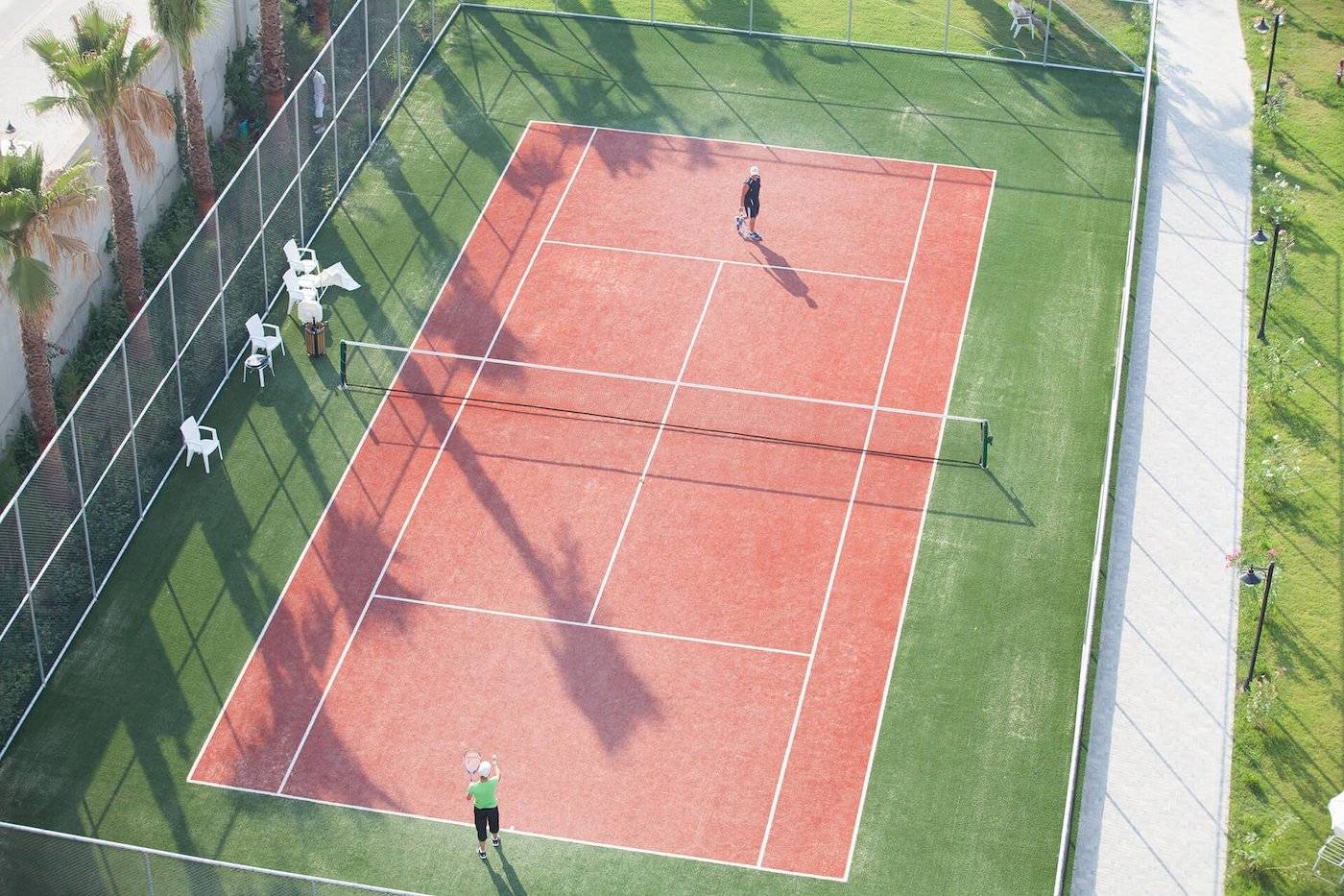 Zwei Personen spielen Tennis auf dem Tennisplatz im Freien im Defne Defnem Hotel.