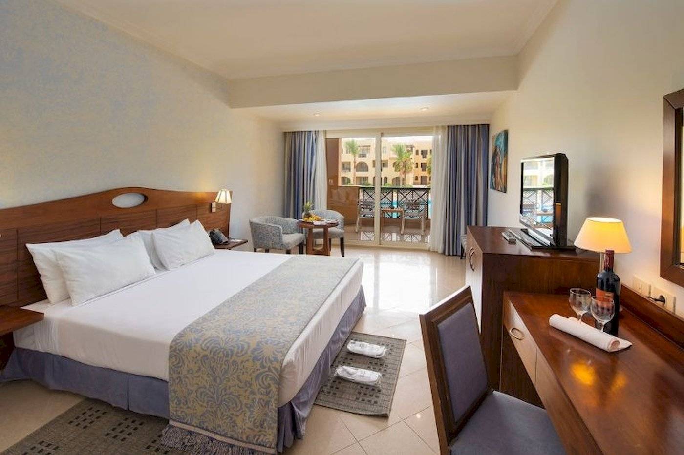 Zimmer im Stella Gardens Resort & Spa Makadi Bay mit Bett, Schreibtisch und Balkonzugang.