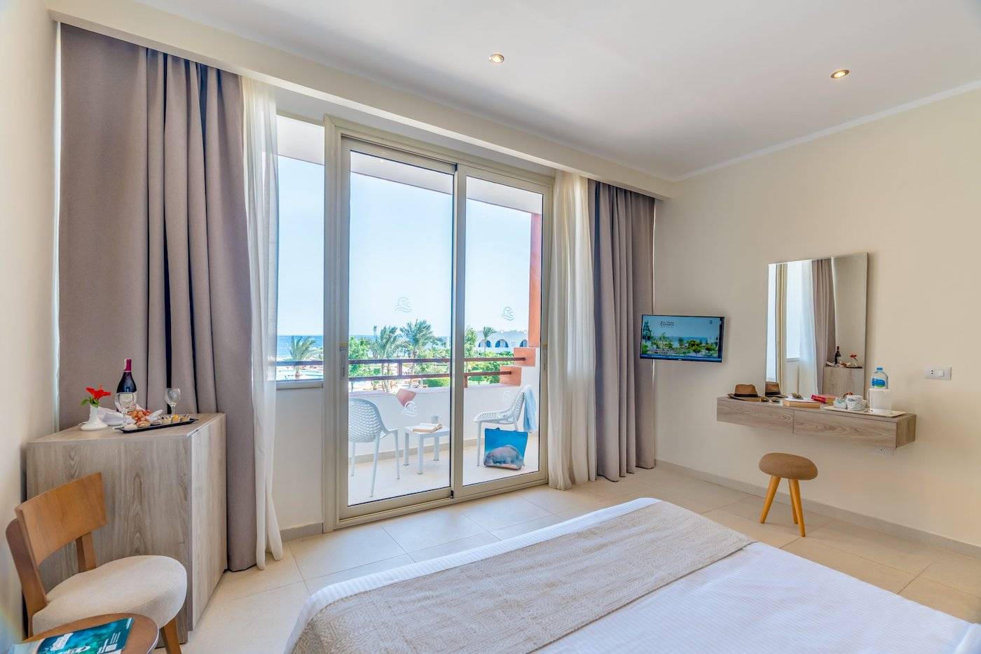 Innenansicht eines Zimmers im Three Corners Equinox Beach Resort mit Balkon, Fernseher und Blick auf den Ozean.
