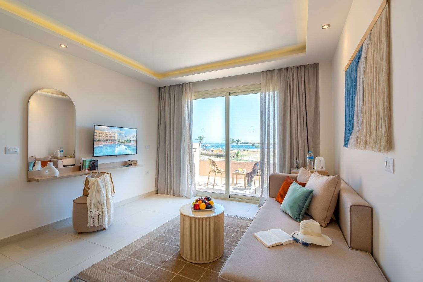 Luxuriöses Zimmer im Three Corners Equinox Beach Resort mit Meerblick, inklusive Wohnzimmer mit Sofa, Tisch, Fernseher, und Balkon.
