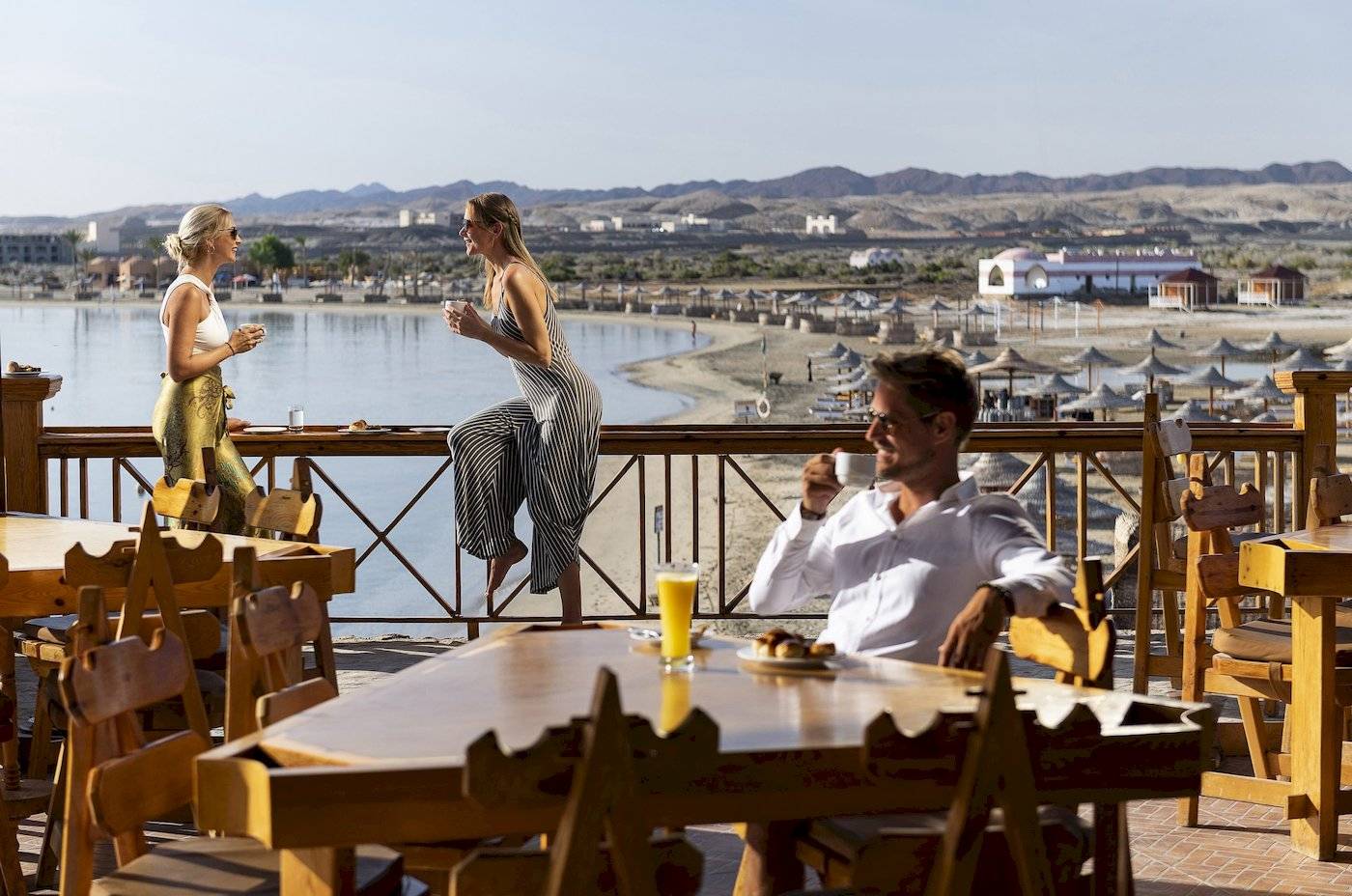 Drei Gäste sitzen auf der Terrasse des Three Corners Equinox Beach Resorts und genießen Getränke und Ausblick.