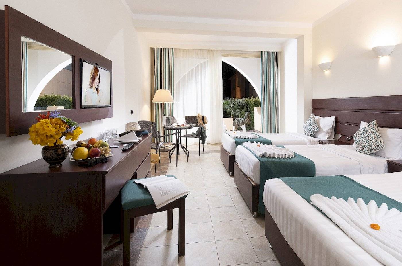 Drei Hotelzimmer im Three Corners Equinox Beach Resort mit Blumen, Obst und bequemen Betten.