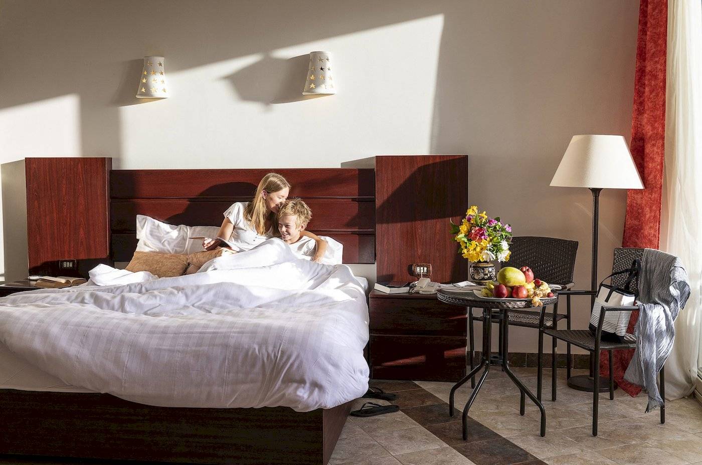 Ein Hotelbettzimmer im Three Corners Equinox Beach Resort mit einer Frau und einem Kind, die im Bett liegen.
