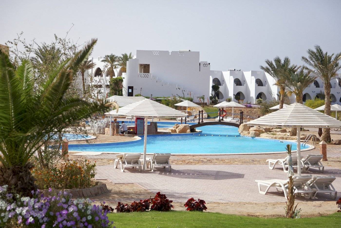 Ein Swimmingpool im Freien mit weißen Sonnenliegen und großen Sonnenschirmen im Three Corners Equinox Beach Resort.