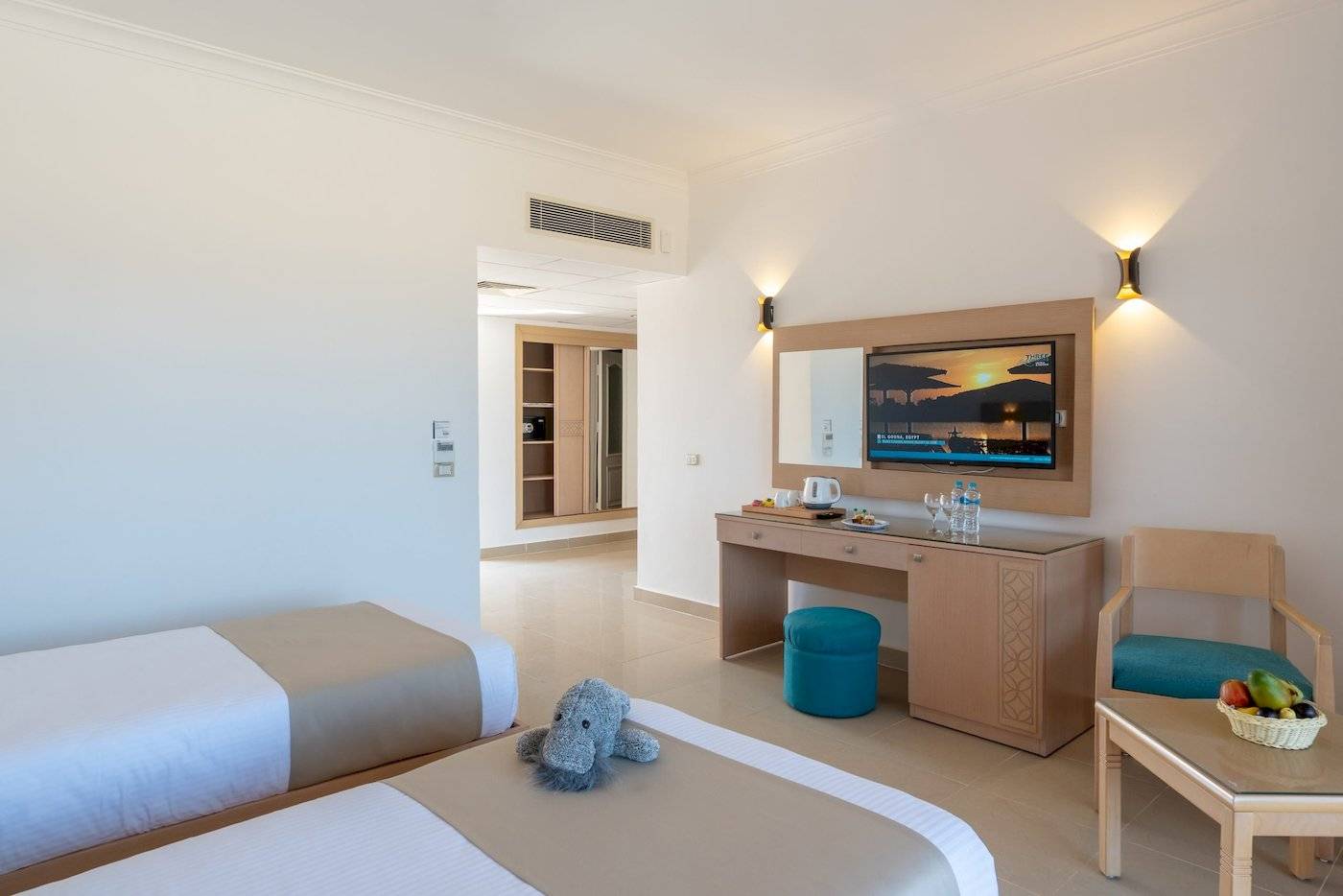 Zimmer im Three Corners Happy Life Beach Resort mit zwei Betten, Schreibtisch, Fernseher und Obstkorb.