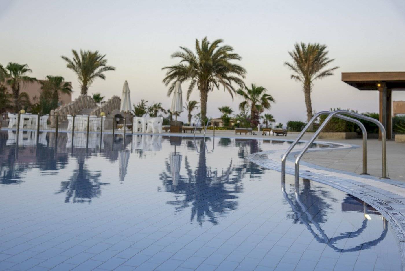 Schwimmbecken im Three Corners Happy Life Beach Resort mit Palmen und Sonnenliegen