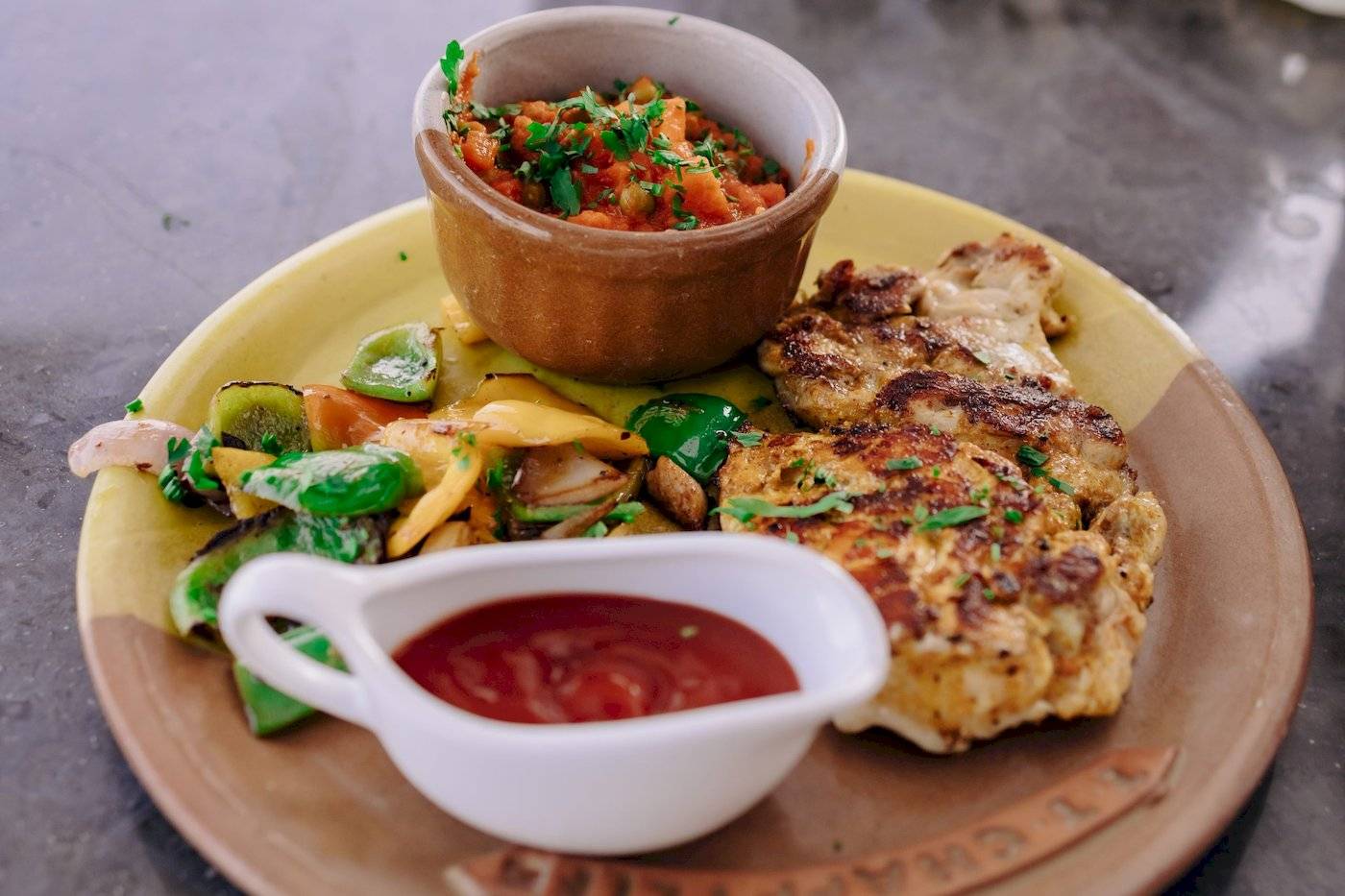 Ein Teller mit gegrilltem Fleisch, gemischten Gemüsen und einer Saucenschüssel.