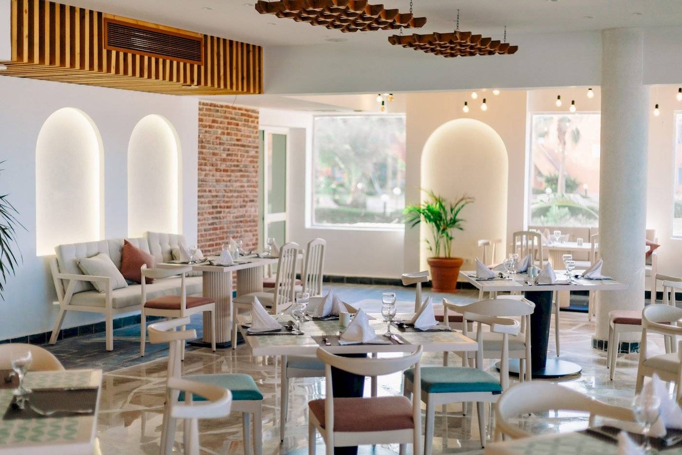 Innenansicht eines Restaurants im Three Corners Happy Life Beach Resort mit weißen Tischen und Stühlen.