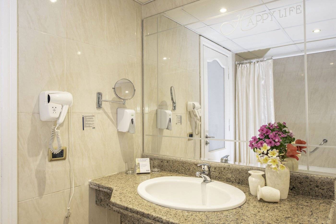 Badezimmer im Three Corners Happy Life Beach Resort mit Spiegel, Waschbecken und Blumenvase.