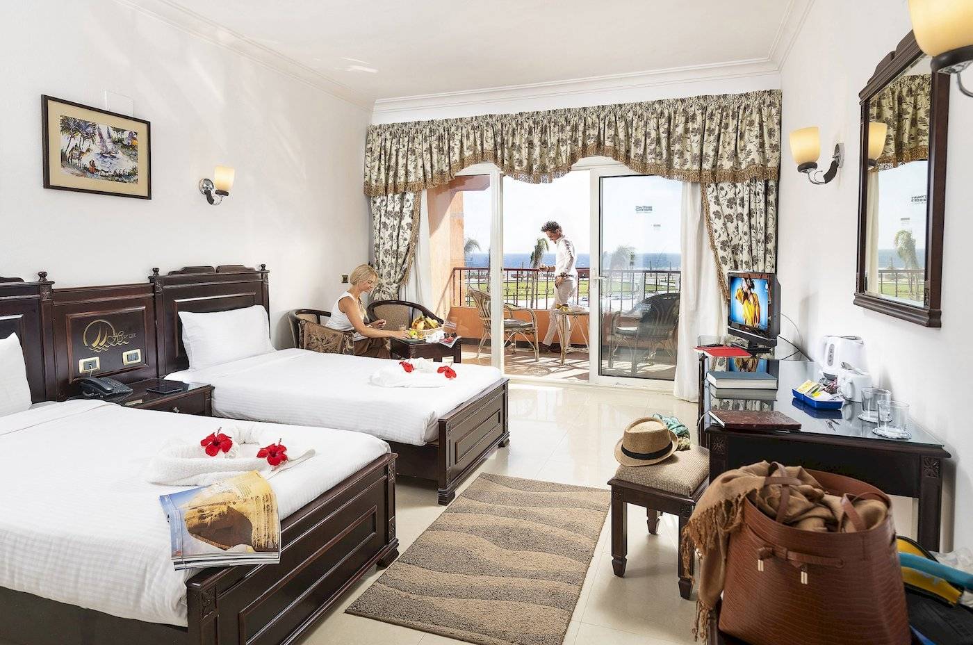 Zimmer im Three Corners Happy Life Beach Resort mit zwei Betten, einem Fernseher, einem Schreibtisch und einer Aussicht auf das Meer.