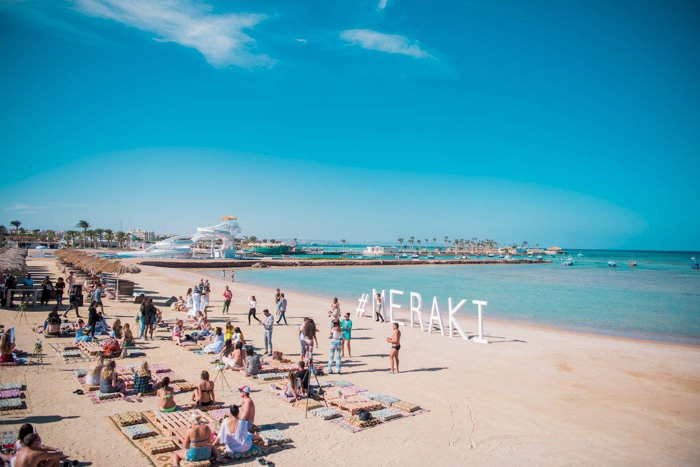 Viele Gäste auf dem Strand vor dem Sunrise Royal Makadi Resort mit großem weißen Schriftzug Merakli