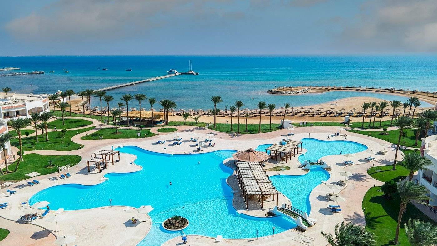 Luftaufnahme des Sunrise Royal Makadi Resorts mit Swimmingpool, Sonnenliegen und Blick aufs Meer.