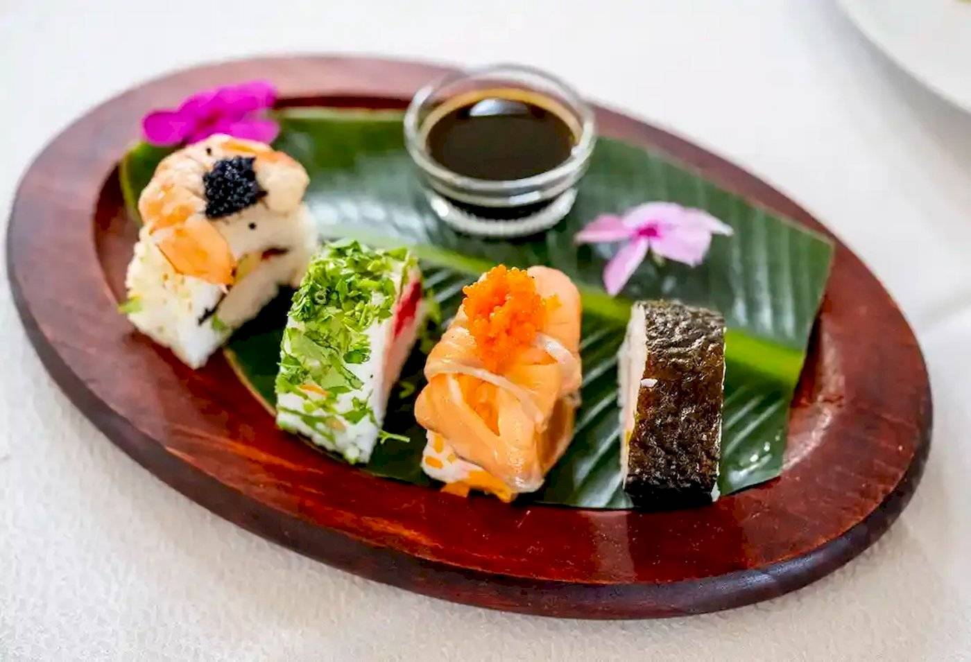 Ein Teller mit verschiedenen Sushi-Variationen auf einem Blatt serviert, mit Sojasauce.