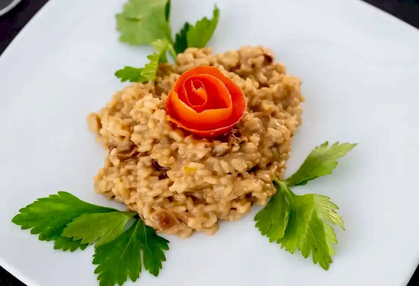 Risotto mit Pilzen und Rose auf einem weißen Teller serviert.