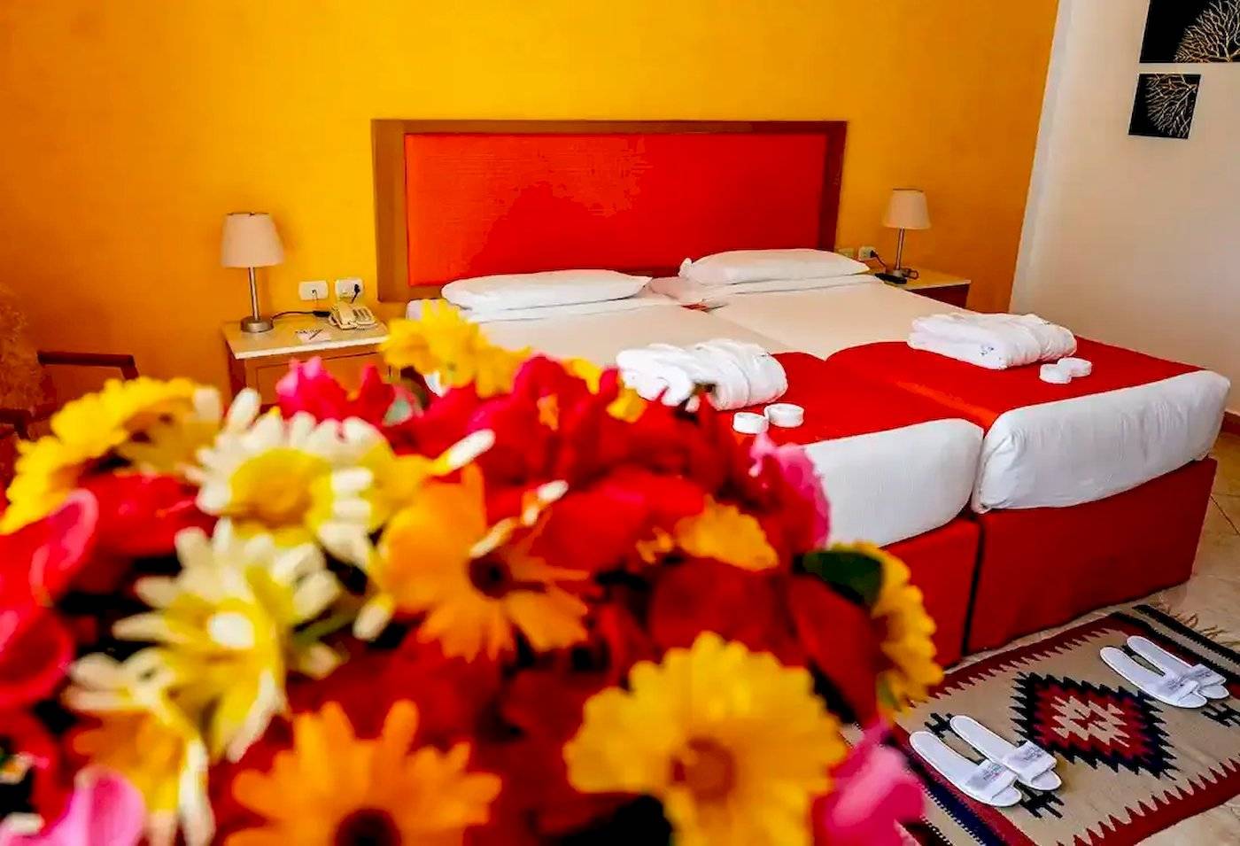 Doppelzimmer im Gorgonia Beach Resort mit zwei Betten, gelben und roten Blumen, und einem roten Kopfteil.