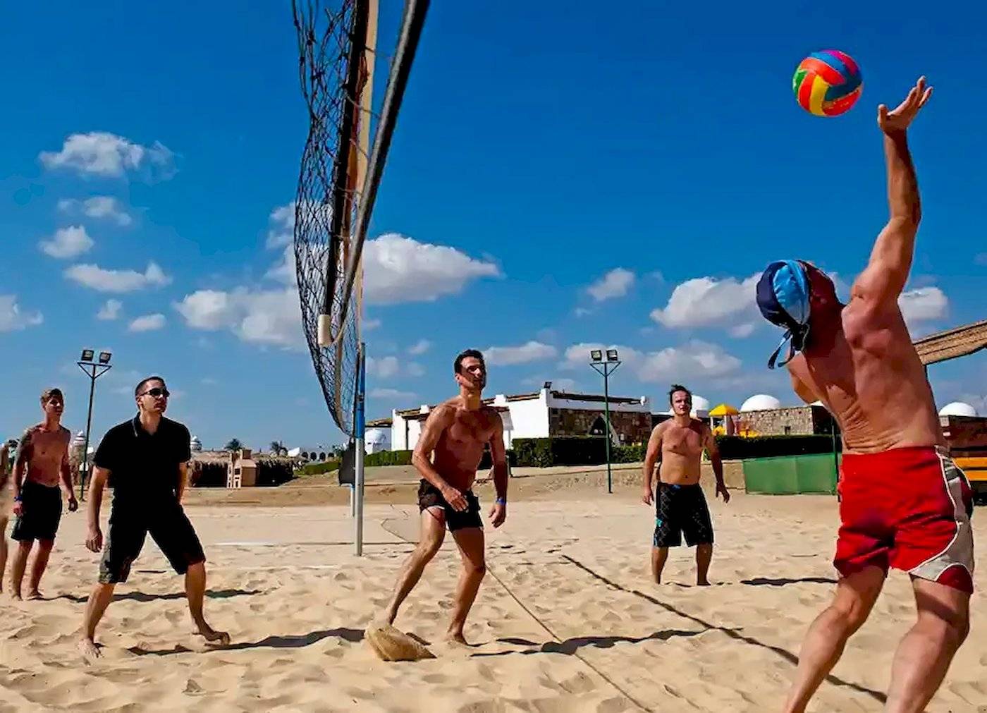 Mehrere Männer spielen Volleyball auf einem Sandstrand in der Nähe eines Hotels.
