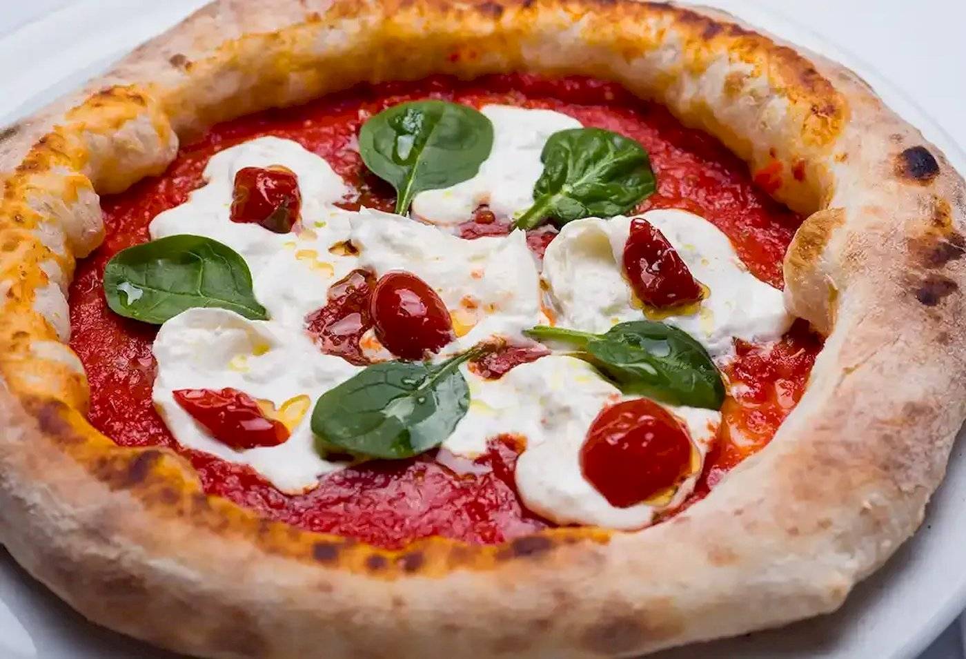 Pizza mit Mozzarella und Spinat auf einem weißen Teller serviert