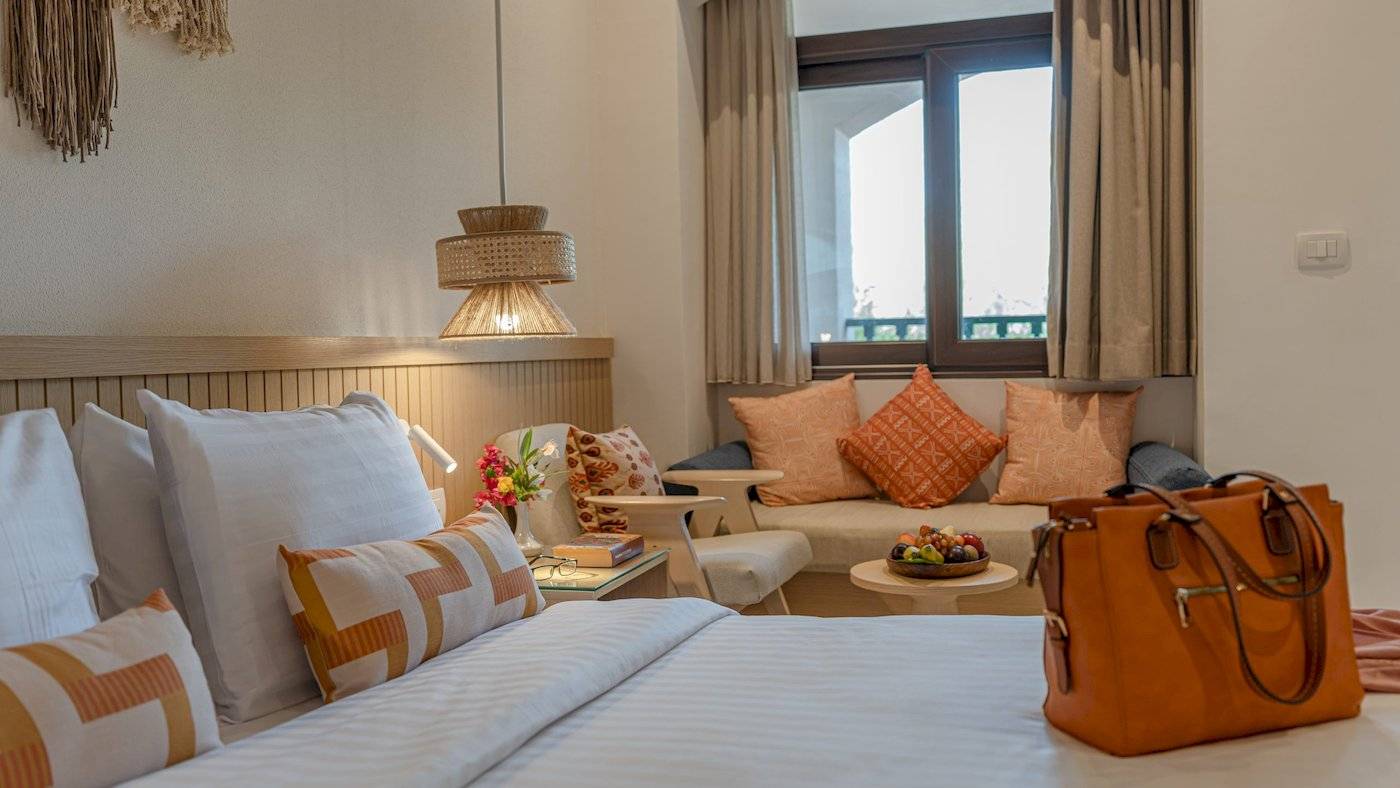 Drei-Ecken-Rihana-Resort-Zimmer mit Bett, Fenster, und Taschen auf dem Bett.