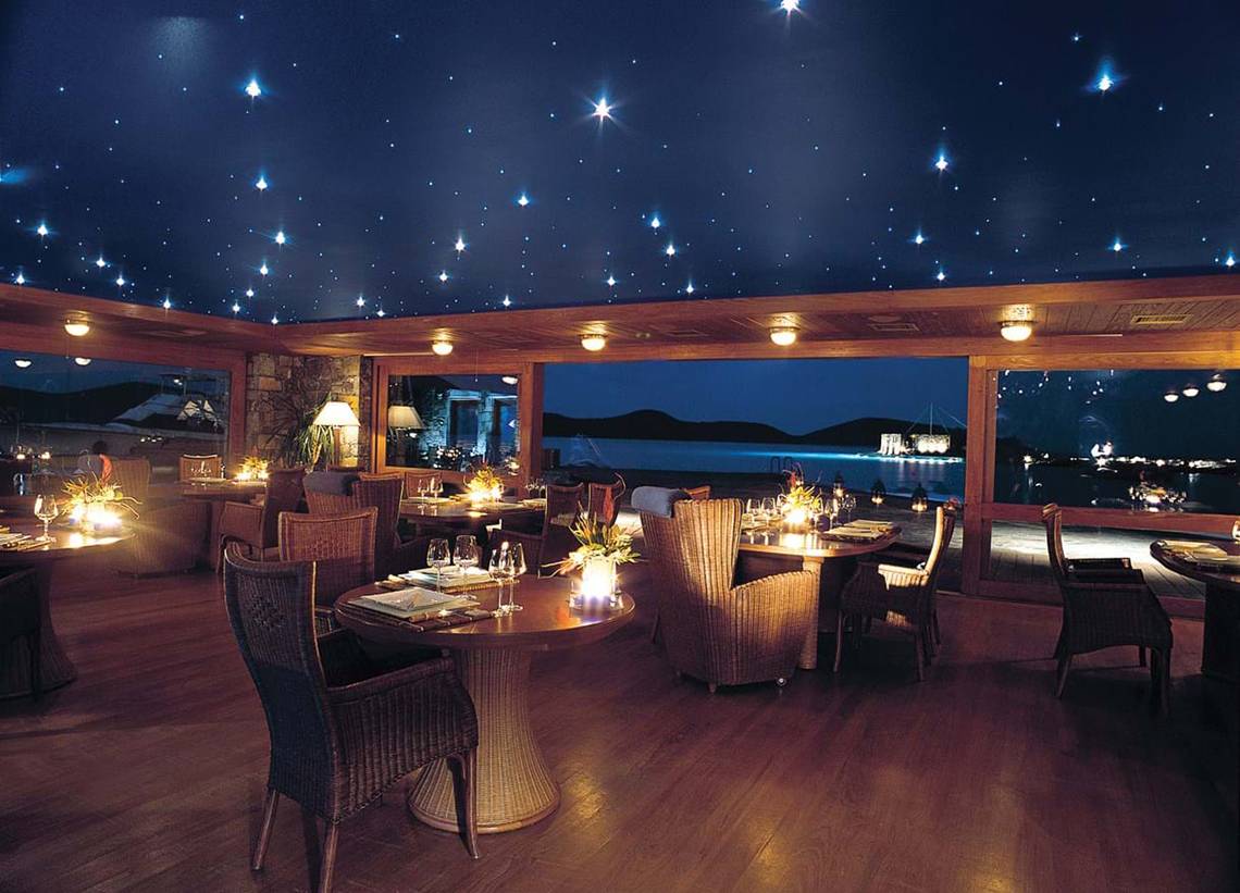 Innenansicht des Restaurants im Elounda Beach Hotel & Villas mit Sternenhimmeldecke und Blick auf den Hafen.