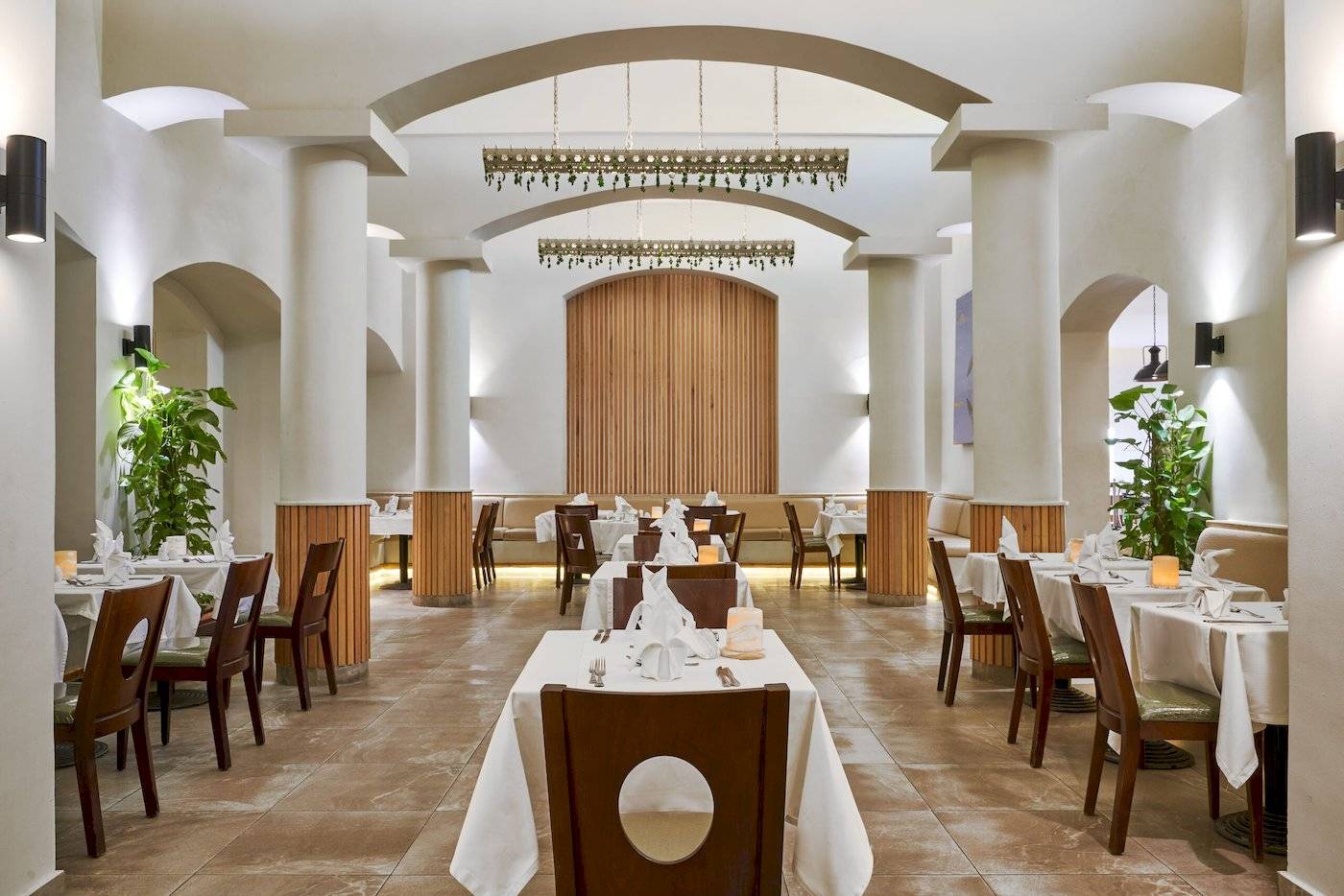 Innenansicht des Restaurants im Three Corners Rihana Resort mit Tisch und Stühlen, weißen Tischdecken, dekorativen Pflanzen und Holzelementen.