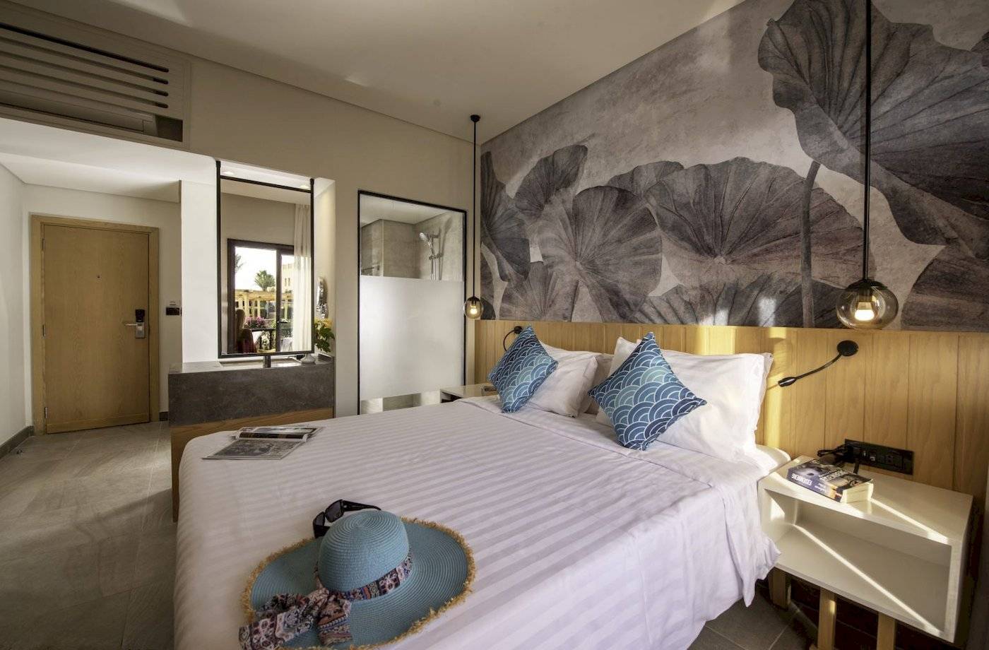 Hotelzimmer im Three Corners Rihana Resort mit Bett, Hut, Büchern und Lampe.