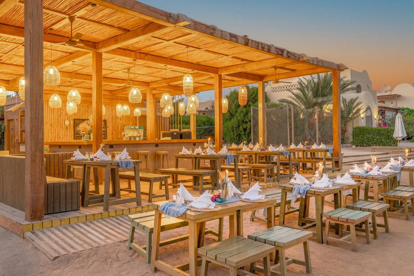 Strandrestaurant des Three Corners Rihana Resorts mit Holztischen und Stühlen, unter einem Strohdach mit Kerzen und Laternen.