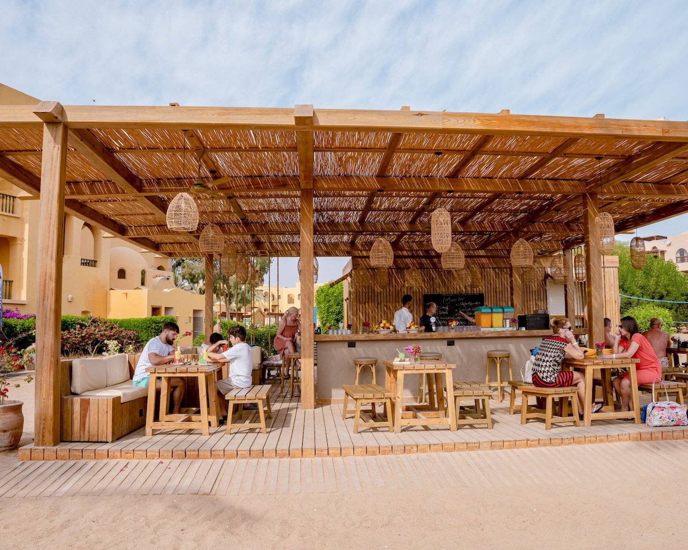 Gäste sitzen an Tischen im Freien unter einem Holzpavillon im Three Corners Rihana Resort.