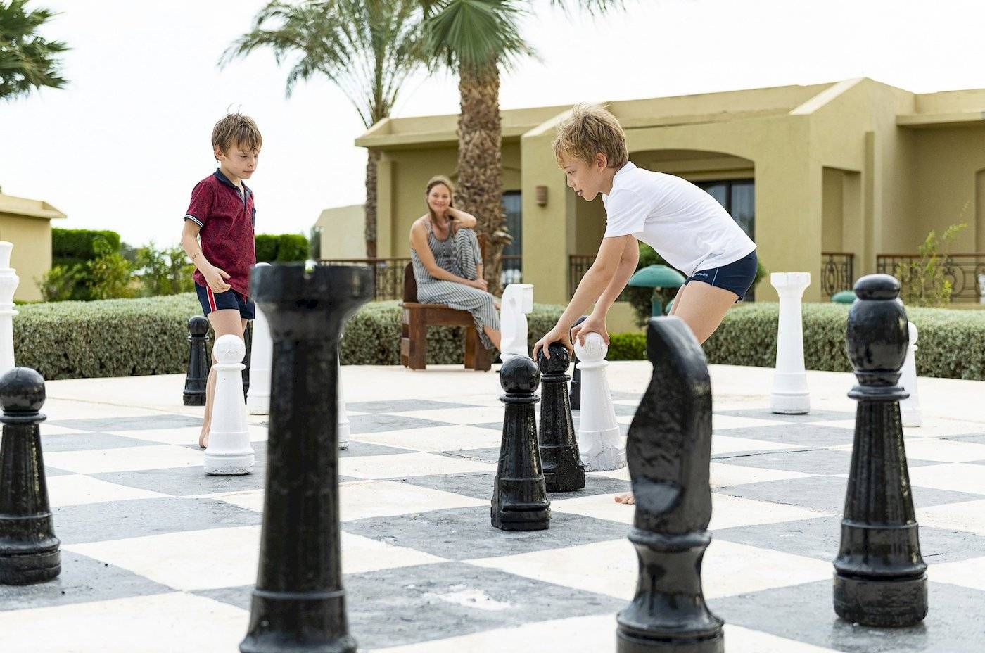 Zwei Kinder spielen Schach im Freien neben einem Hotel.