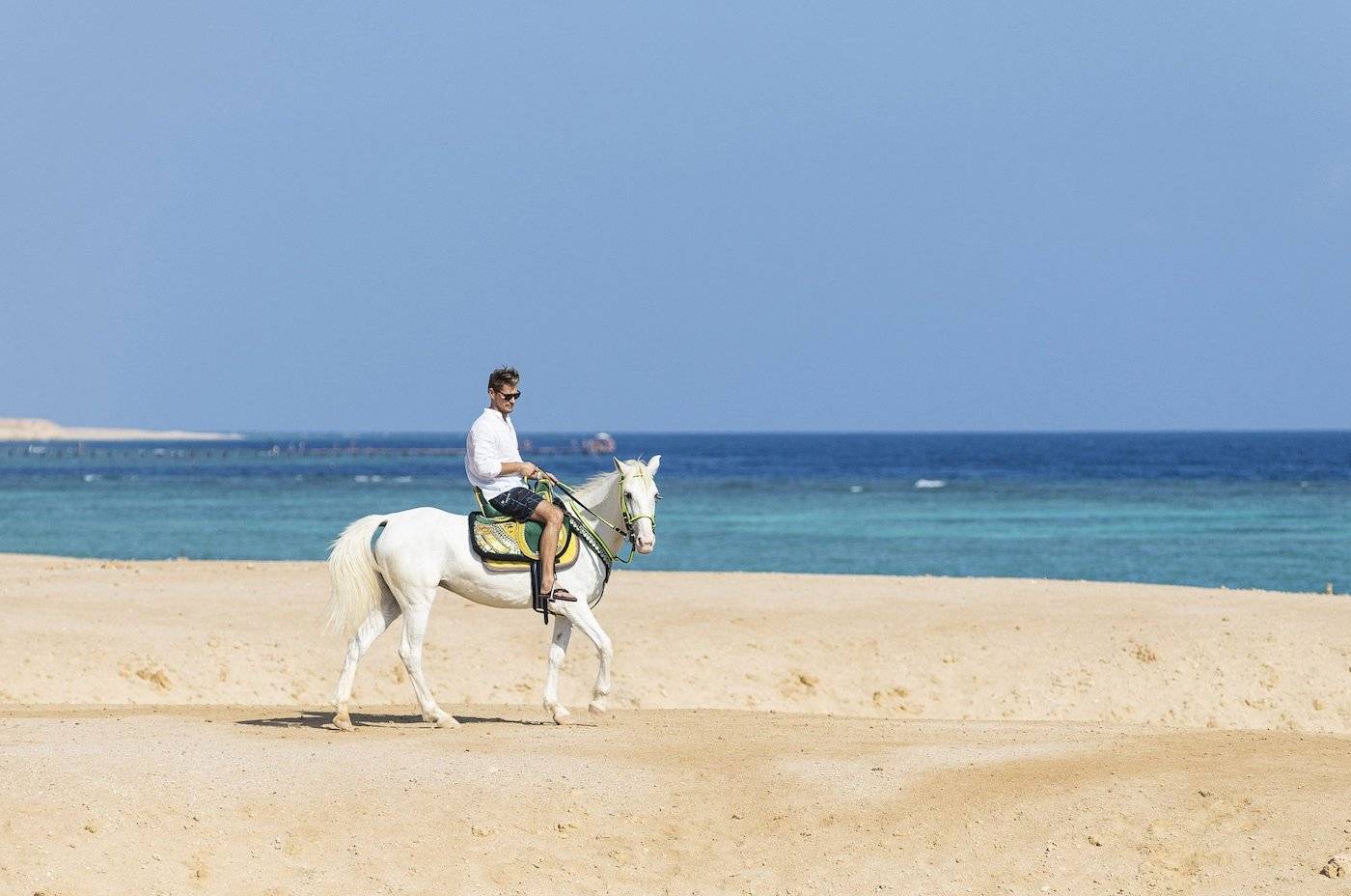 Ein Mann reitet auf einem weißen Pferd auf dem Strand des Three Corners Fayrouz Plaza Beach Resort.