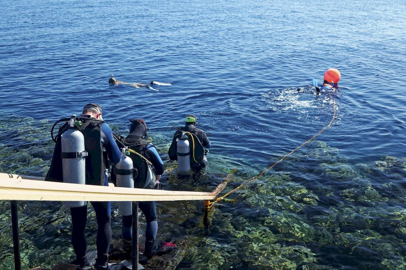 Scuba-Taucher in Schutzausrüstung, die das Meer betreten, um zu tauchen.