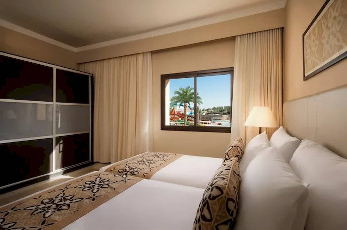 Hotelzimmer im JAZ Neo Dar El Madina mit zwei Betten, Fenster und Ausblick auf Wasserrutschen.