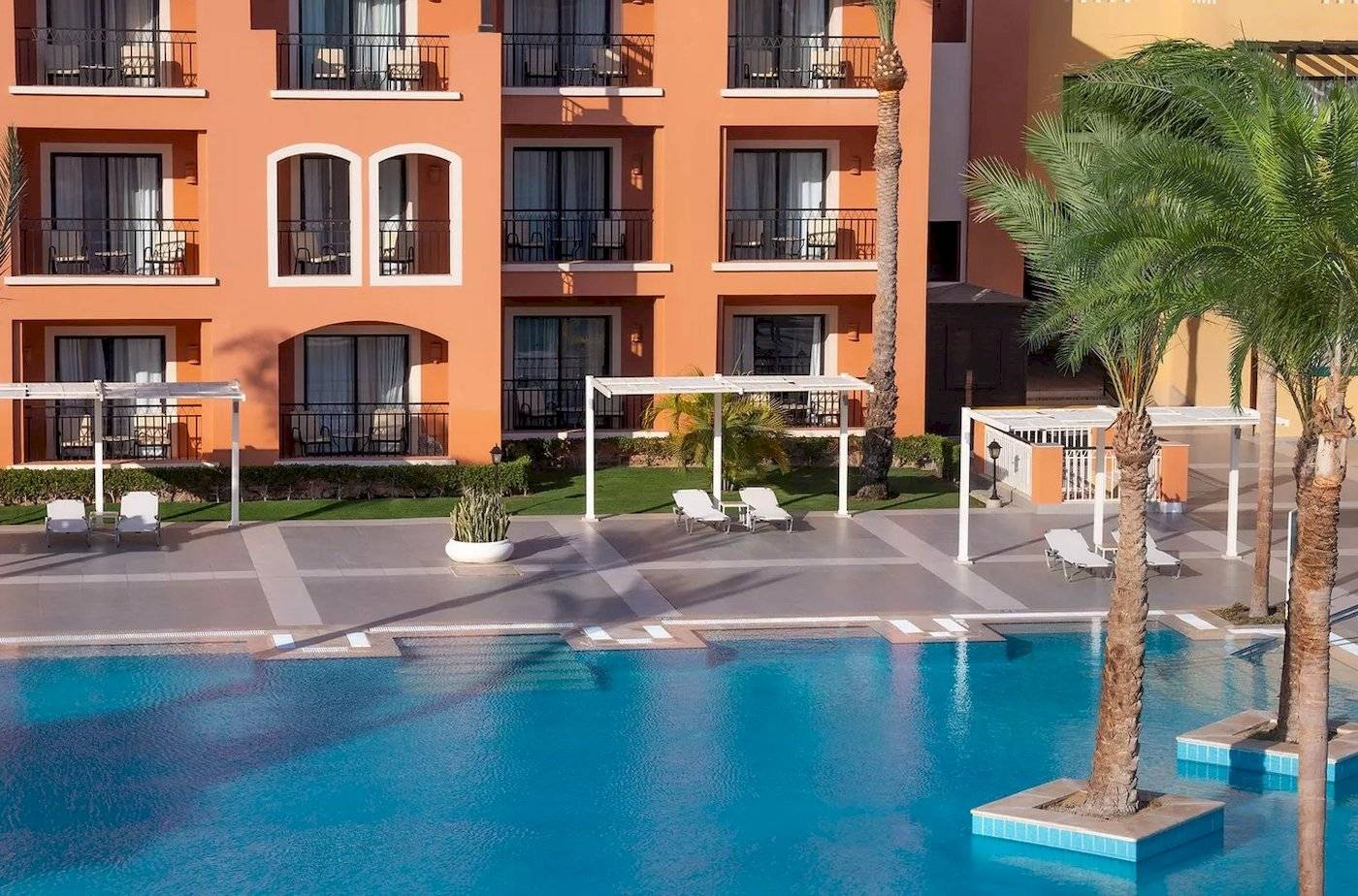 Außenbereich des JAZ Neo Dar El Madina Hotels mit Swimmingpool und Sonnenliegen.